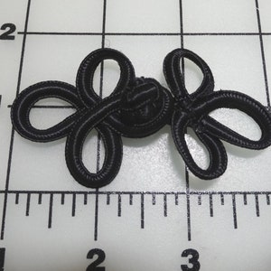 May include: Black fabric knot closure with a decorative design. The knot is about 1 inch in diameter.