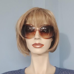 May include: A brown and gold pair of oversized sunglasses with a rounded, cat-eye shape. The sunglasses are on a mannequin with short, brown hair.