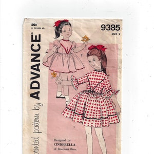 May include: Vintage sewing pattern for a girl's dress. The pattern is for a dress with a red and white print and a pink dress with a red trim. The pattern is from Advance, a printed pattern by Cinderella of Rosenau Bros. The pattern number is 9385, size 2.