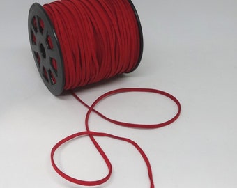 May include: A spool of red suede cord with a black plastic bobbin. The cord is unwound and laid out in a loop.