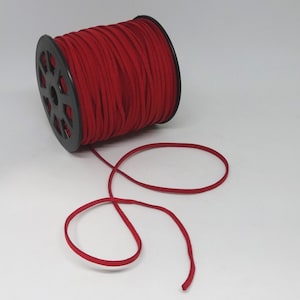 Può includere: Un rocchetto di cordoncino in pelle scamosciata rosso con una bobina in plastica nera. Il cordoncino è srotolato e disposto in un anello.