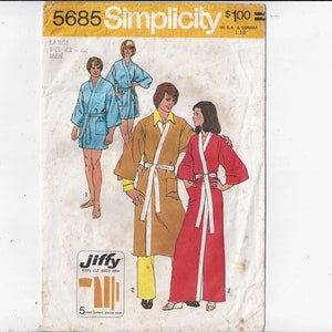Könnte beinhalten: Simplicity-Schnittmuster Nummer 5685 für eine Robe. Das Schnittmuster zeigt drei Personen, die Roben in verschiedenen Farben tragen: blau, braun und rot. Das Schnittmuster trägt den Titel "Jiffy" und enthält Anweisungen zum Nähen einer Robe mit einem "schnellen Schnitt" und einem "leicht zu nähenden" Design.