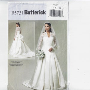Puede incluir: Un patrón de costura Butterick, B5731, que presenta un vestido de novia blanco con mangas largas de encaje, un escote en V y una falda amplia. El patrón incluye una pieza de corpiño separada para tallas de copa A/B, C, D. La imagen muestra a una mujer con el vestido.