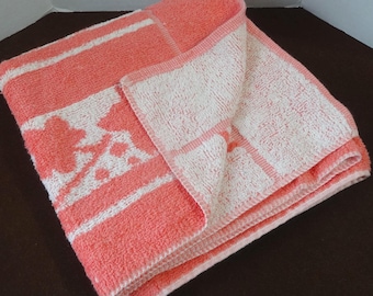 May include: A pink and white bath towel with a white pattern of stylized hearts and flowers. The towel is folded in half and the white side is facing up.