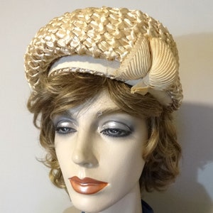 May include: A cream-colored straw hat with a large, folded bow on the side. The hat is made of woven straw and has a wide brim.