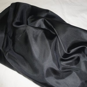 May include: Black fabric with a smooth, silky texture. The fabric is draped and folded, showing its sheen and drape.
