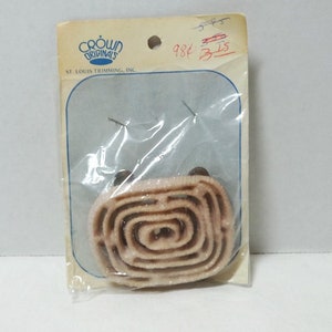 May include: A package of beige elastic trim with two metal snaps. The package is labeled "Crown Originals" and "St. Louis Trimming, Inc.". The price is marked as "98¢".