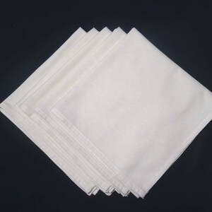May include: A stack of six white cotton napkins, folded in a square shape.