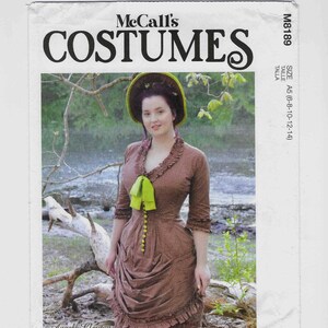 May include: A McCall's Costumes pattern envelope featuring a woman in a brown dress with a green bow. The text "COSTUMES" is prominently displayed above the image. The pattern is labeled M8189 and includes size information.
