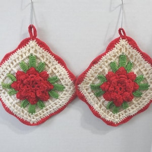 May include: A pair of crocheted pot holders with a red flower design in the center. The pot holders are white with a red border.