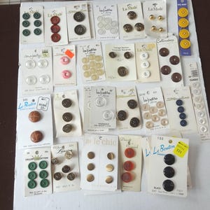 Könnte beinhalten: Eine Sammlung von Vintage-Knöpfen in verschiedenen Farben und Stilen, darunter Grün, Braun, Gold und Schwarz. Die Knöpfe werden auf ihren Originalkarten präsentiert und zeigen verschiedene Größen und Designs. Einige Karten haben Text.