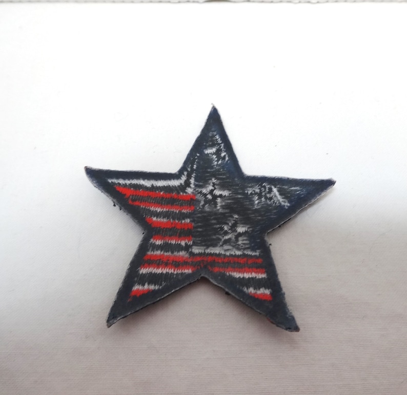 Pode incluir: Um remendo azul em forma de estrela com um design de bandeira americana vermelha, branca e azul.