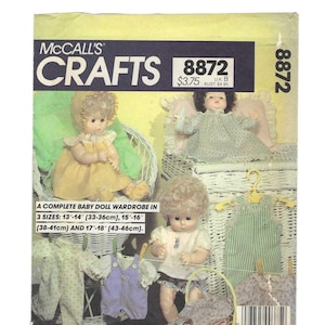 May include: McCall's Crafts pattern 8872 for a complete baby doll wardrobe. The image shows three baby dolls with various outfits, including dresses and overalls. The pattern includes sizes for 13"-14", 15"-16", and 17"-18" dolls.