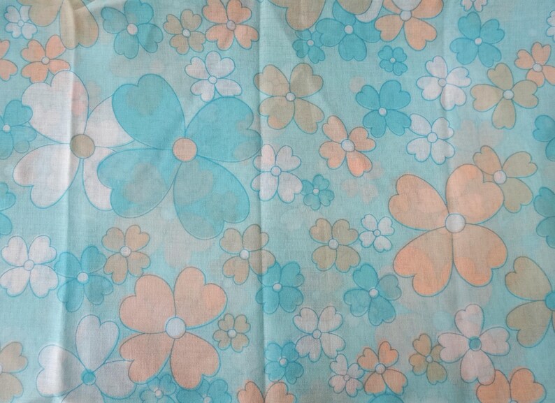 May include: A fabric with a repeating floral pattern. The flowers are in shades of blue, peach, white, and tan, set against a light blue background. The flowers have a retro, stylized design, with rounded petals and a central dot.