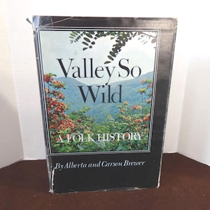 May include: A black book with the title "Valley So Wild: A Folk History" by Alberta and Carson Brewer. The cover features a photograph of a lush green mountain valley with red flowers.