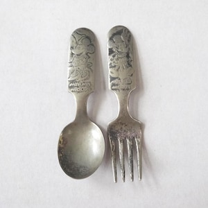 Può includere: Set vintage di cucchiaio e forchetta color argento con Topolino e Minnie. Il cucchiaio ha una forma arrotondata, e la forchetta ha quattro rebbi. Entrambi gli utensili presentano un design in rilievo dettagliato dei personaggi e le parole "Minnie Mouse".