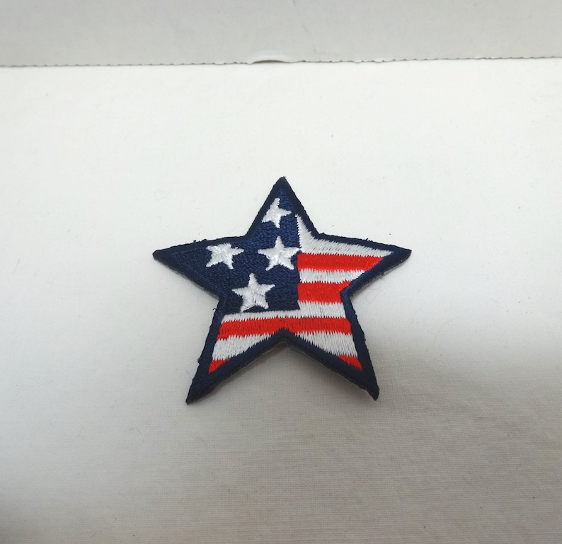 Pode incluir: Um remendo azul em forma de estrela com um design de bandeira americana vermelha, branca e azul.