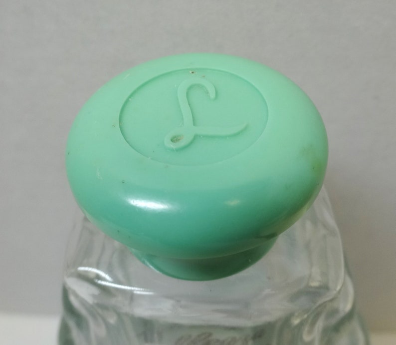 May include: A clear glass bottle with a green plastic lid. The lid has a raised letter "L" on it.