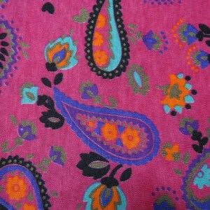 May include: A pink fabric with a paisley pattern in shades of blue, purple, orange, and black.