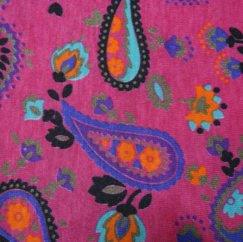 May include: A pink fabric with a paisley pattern in shades of blue, purple, orange, and black.