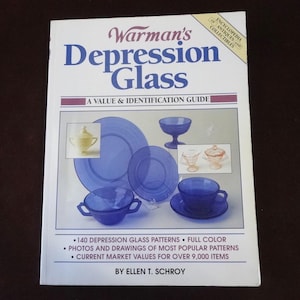 May include: A book titled "Warman's Depression Glass: A Value & Identification Guide" by Ellen T. Schroy. The cover features a collection of blue depression glass, including a bowl, a plate, a cup and saucer, and a sugar bowl.