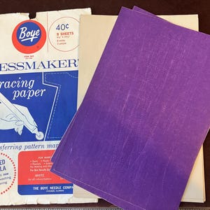 May include: A package of Boye dressmaker's tracing paper containing 9 sheets, measuring 8.5 by 12.5 inches, with 6 white and 3 purple sheets. The packaging features blue, white, and red graphics with text including 'tracing paper' and 'improved formula'.