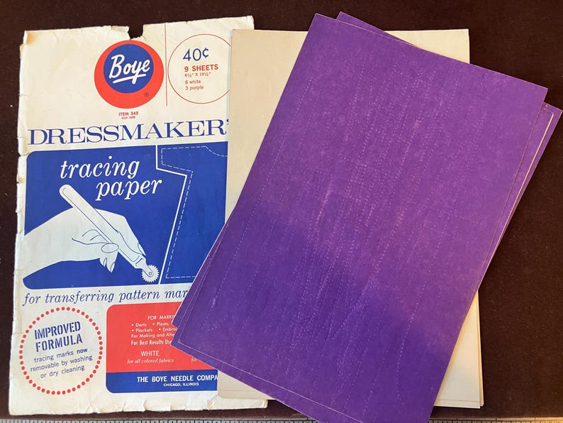 May include: A package of Boye dressmaker's tracing paper containing 9 sheets, measuring 8.5 by 12.5 inches, with 6 white and 3 purple sheets. The packaging features blue, white, and red graphics with text including 'tracing paper' and 'improved formula'.