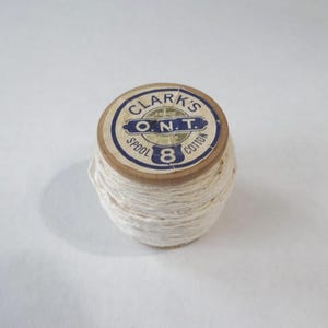 Puede incluir: Una bobina de hilo blanco con una etiqueta que dice "Clark's O.N.T. Spool 8 Cotton".