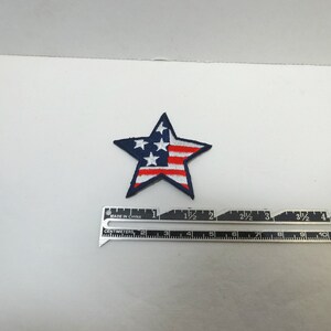 Pode incluir: Um remendo azul em forma de estrela com um design de bandeira americana vermelha, branca e azul. O remendo tem aproximadamente 3,8 cm de largura.
