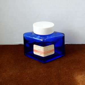 May include: A small, cobalt blue glass bottle of New Parker's Super Quink permanent red ink with a white plastic lid.