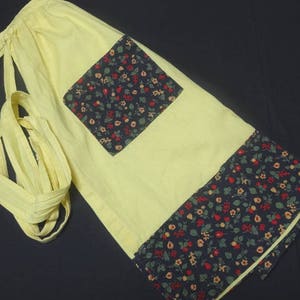 May include: A yellow apron with a black and white floral print. The apron has a large pocket on the front and ties at the waist.