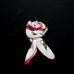 May include: A white scarf with a pink border and a floral print in shades of pink, blue, and green. The scarf is folded and tied into a knot.