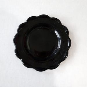May include: A black, scalloped-edge saucer with a smooth, glossy finish.