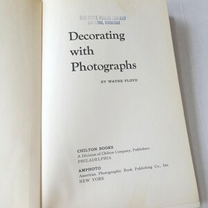 Könnte beinhalten: Offenes Buch mit dem Titel "Decorating with Photographs" von Wayne Floyd. Veröffentlicht von Chilton Books und Amphoto. Der Einband ist cremefarben mit schwarzem Text. Ein Bibliotheksstempel ist oben sichtbar.