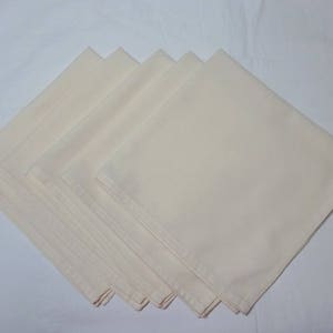 May include: A stack of six off-white linen napkins. The napkins are folded in half and stacked on top of each other.