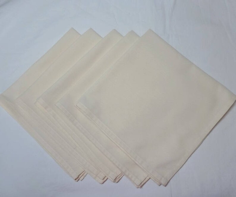 May include: A stack of six off-white linen napkins. The napkins are folded in half and stacked on top of each other.