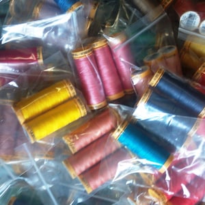 May include: A selection of colourful thread spools in clear plastic bags. The spools are arranged in a random pattern and are mostly red, yellow, blue, and green.