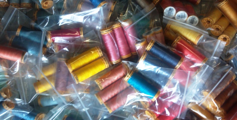 K&ouml;nnte beinhalten: Eine Vielzahl von bunten Garnrollen in durchsichtigen Plastikt&uuml;ten. Die Rollen sind in einem zuf&auml;lligen Muster angeordnet und sind haupts&auml;chlich rot, gelb, blau und gr&uuml;n.