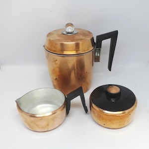 May include: A vintage copper coffee percolator with a black handle and lid, and a glass knob. The set includes a creamer and a lid. The coffee pot is approximately 10 inches tall.
