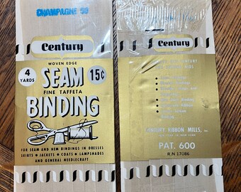 Puede incluir: Dos paquetes de cinta de unión de borde tejido Century en tafetán fino. Los paquetes son dorados y blancos con rayas negras y blancas. El texto en los paquetes dice "Century Woven Edge Seam Binding Fine Taffeta 4 Yards 15c 100% Rayon Pat. 600 RN 17086".