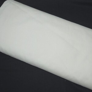 May include: A large, folded piece of white fabric, possibly cotton or linen, is displayed against a dark background. The fabric is smooth and appears to be freshly pressed, with subtle folds and shadows adding depth to the image.