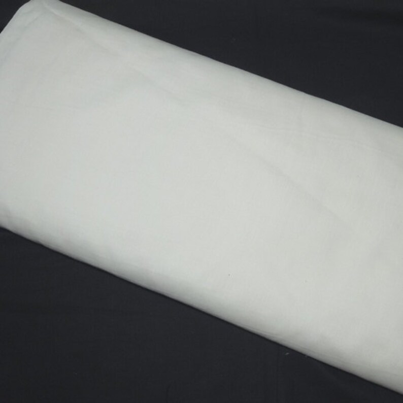May include: A large, folded piece of white fabric, possibly cotton or linen, is displayed against a dark background. The fabric is smooth and appears to be freshly pressed, with subtle folds and shadows adding depth to the image.