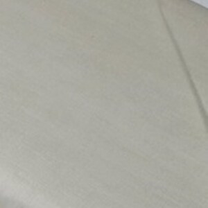 May include: A close-up shot of a light beige fabric with subtle texture. The fabric appears to be smooth and possibly linen or a similar material. The lighting creates soft shadows across the surface.
