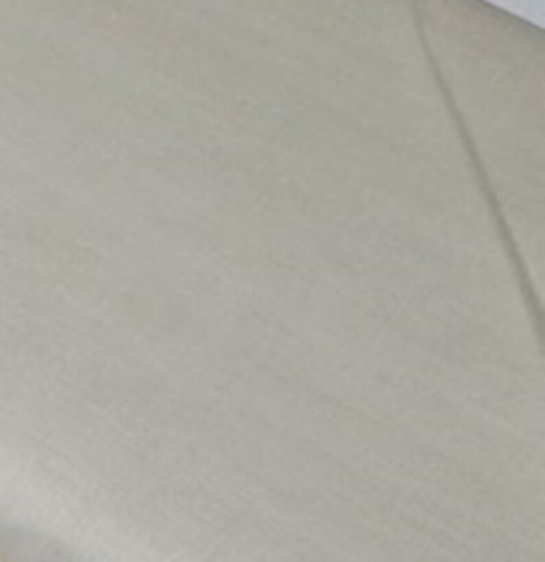 May include: A close-up shot of a light beige fabric with subtle texture. The fabric appears to be smooth and possibly linen or a similar material. The lighting creates soft shadows across the surface.