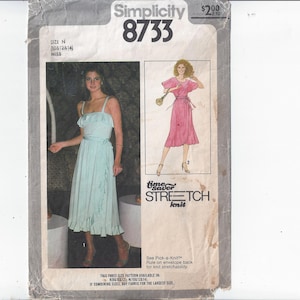 May include: Vintage Simplicity sewing pattern 8733. The pattern envelope features illustrations of two dresses. One is a light blue midi dress with a ruffled neckline and hem. The other is a pink dress with a wrap-style design. The text "time saver stretch knit" is visible.