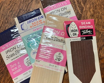 May include: Three packages of iron-on seam binding in navy, beige, and toast colors. The packages feature a vintage design with an iron and the text "Iron-On Seam Binding". The beige package has the text "Non-Shrink Guaranteed Color Fast" and the navy package has the text "Turn a hem in minutes". The toast package has the text "Seam Binding Talon Tapes" and the text "3 yards 35c".