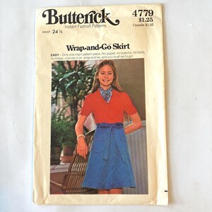 May include: A Butterick 4779 sewing pattern envelope for a Wrap-and-Go Skirt. The cover features a photograph of a blue wrap skirt with a tie waist and patch pockets, paired with a red short-sleeved top. The text includes the pattern number 4779.