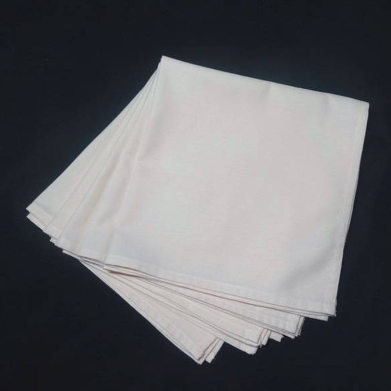 May include: A stack of 10 white cotton napkins, folded in half, with a soft, smooth texture.