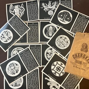 May include: A collection of black and white informational cards depicting Mississippian culture gorgets with titles like The Serpent, The Turkeys, and The Sacred Fire, accompanied by a brown paper bag labeled Cherokee Trading Post, El Reno, Okla.