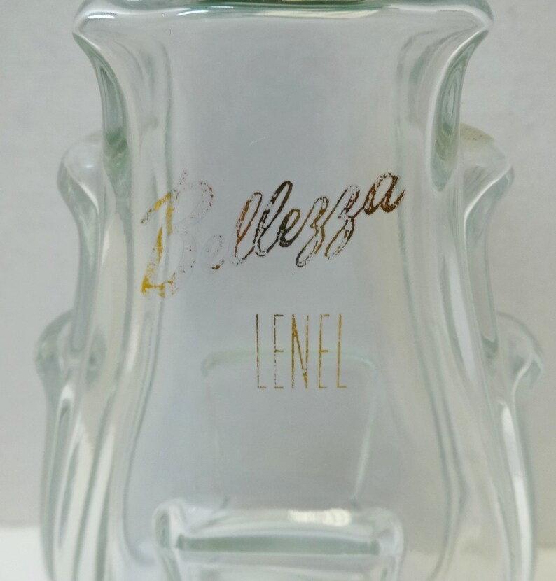 May include: A clear glass bottle with a textured surface. The bottle has a gold label with the text "Bellezza Lenel" on it.